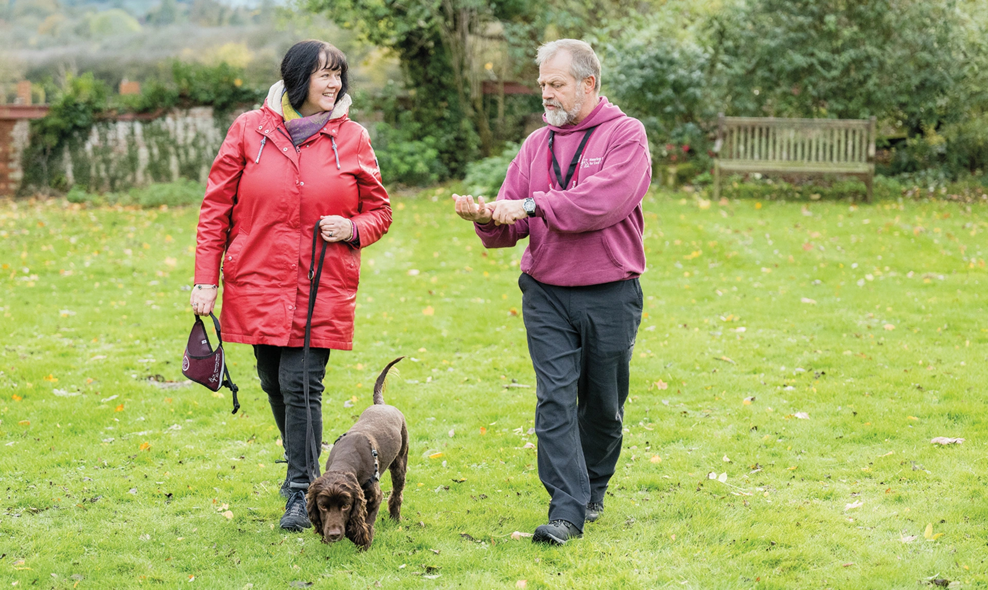 A man in hearing dogs staff uniform talking to and walking with a woman with a hearing dog