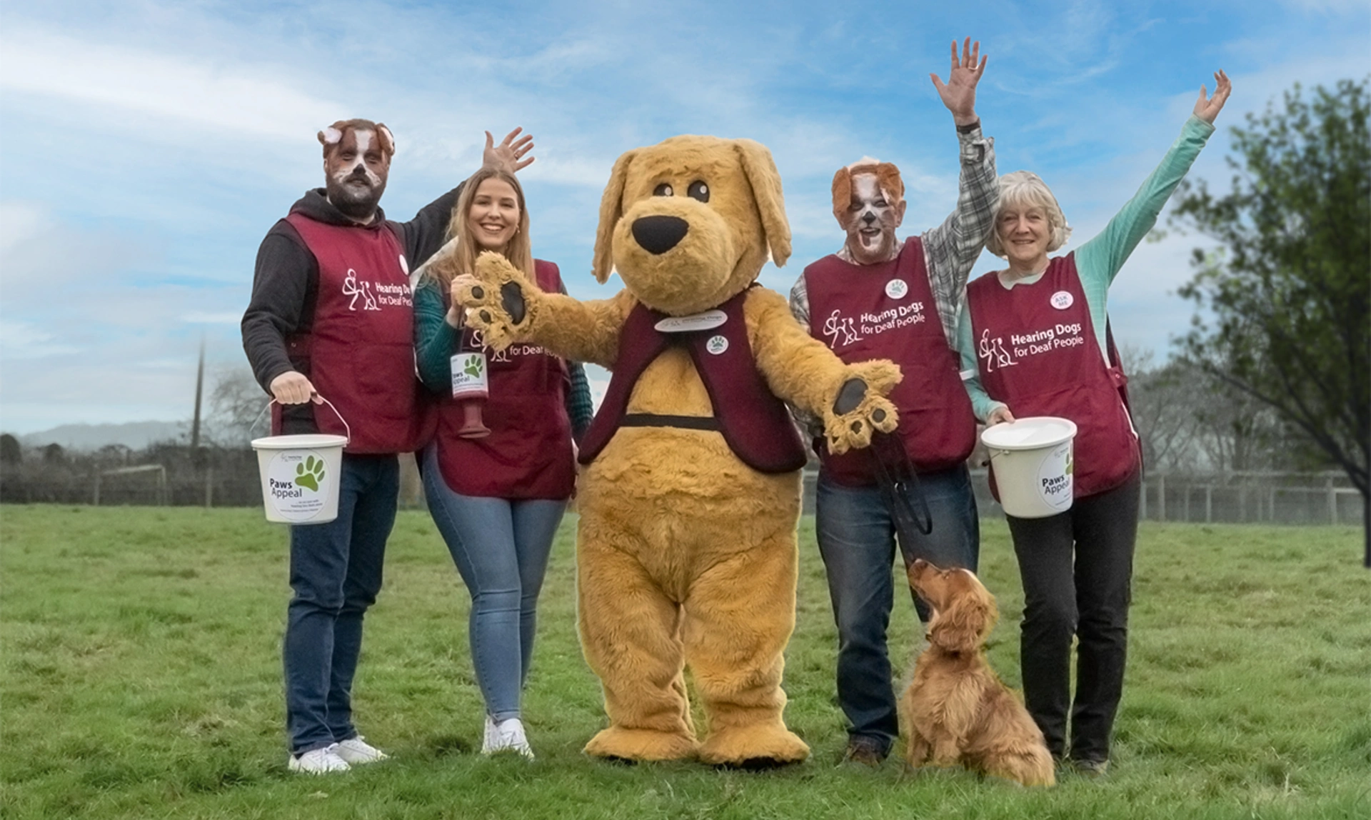 Group of people and a dog mascot looks happy with collection buckets outside