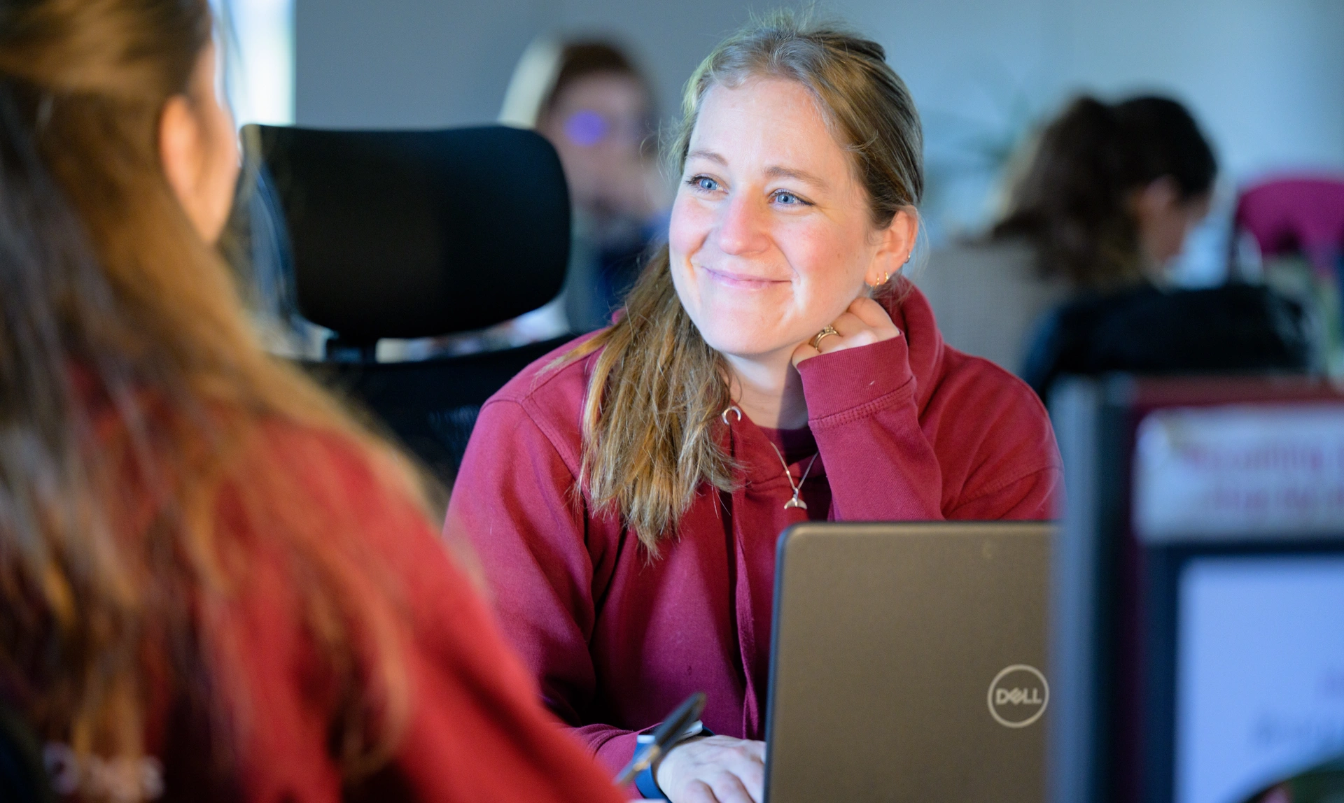 A member of hearing dogs staff sat at a desk with a computer in front of her looking up and smiling