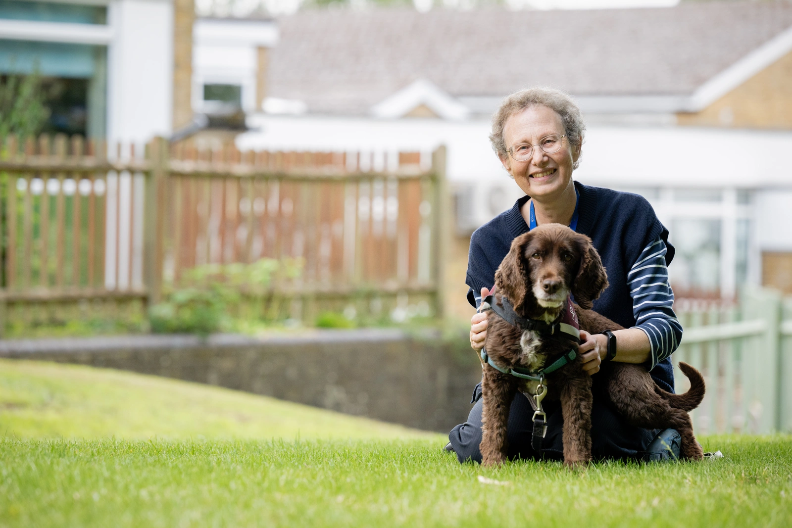 A smiling woman and a brown dog pose for the photo on a grassy area.