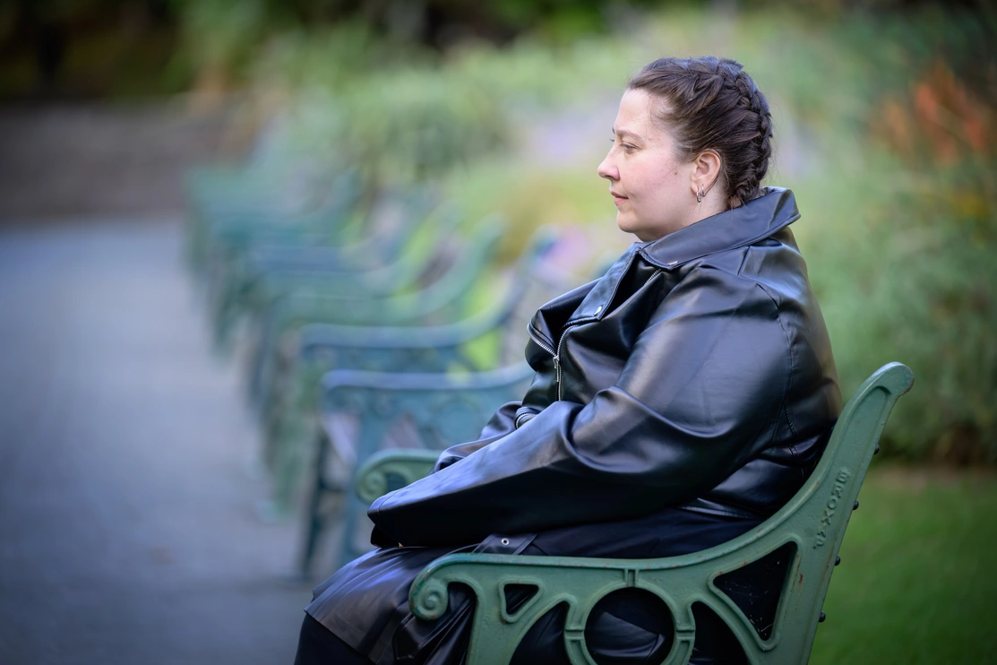 A woman in a leather coat is sitting on a park bench