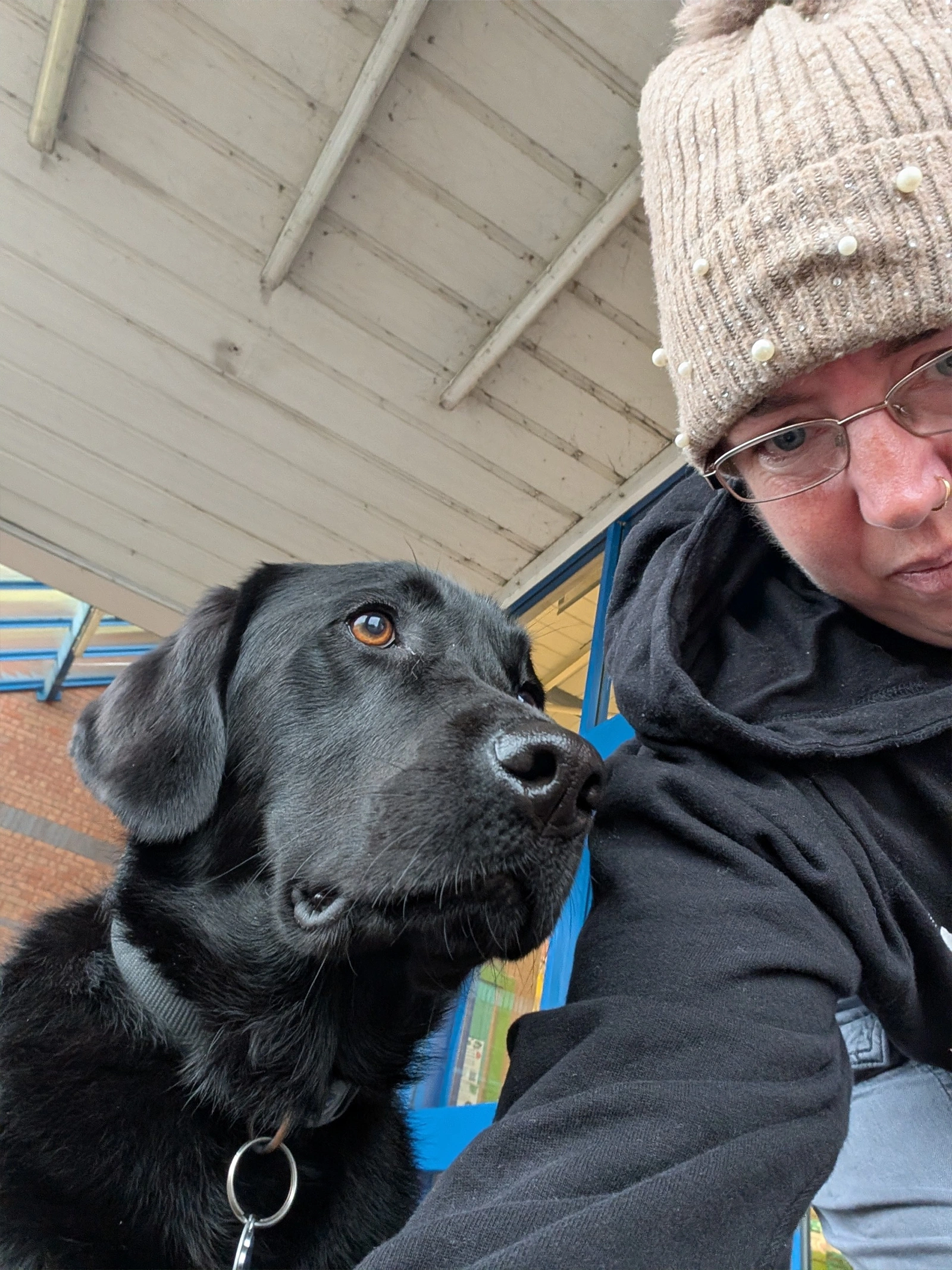 A selfie of a black Labrador and a lady wearing a hat