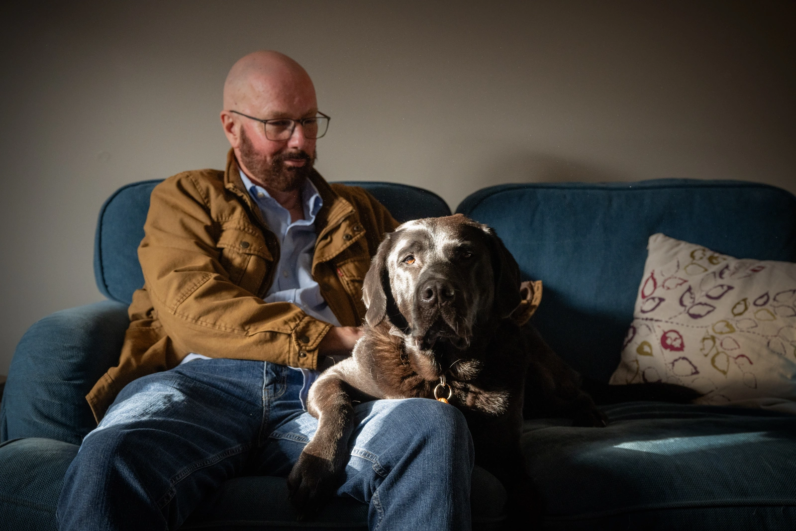 A bearded man, trevor sitting on a sofa with a large brown and white dog on his lap.