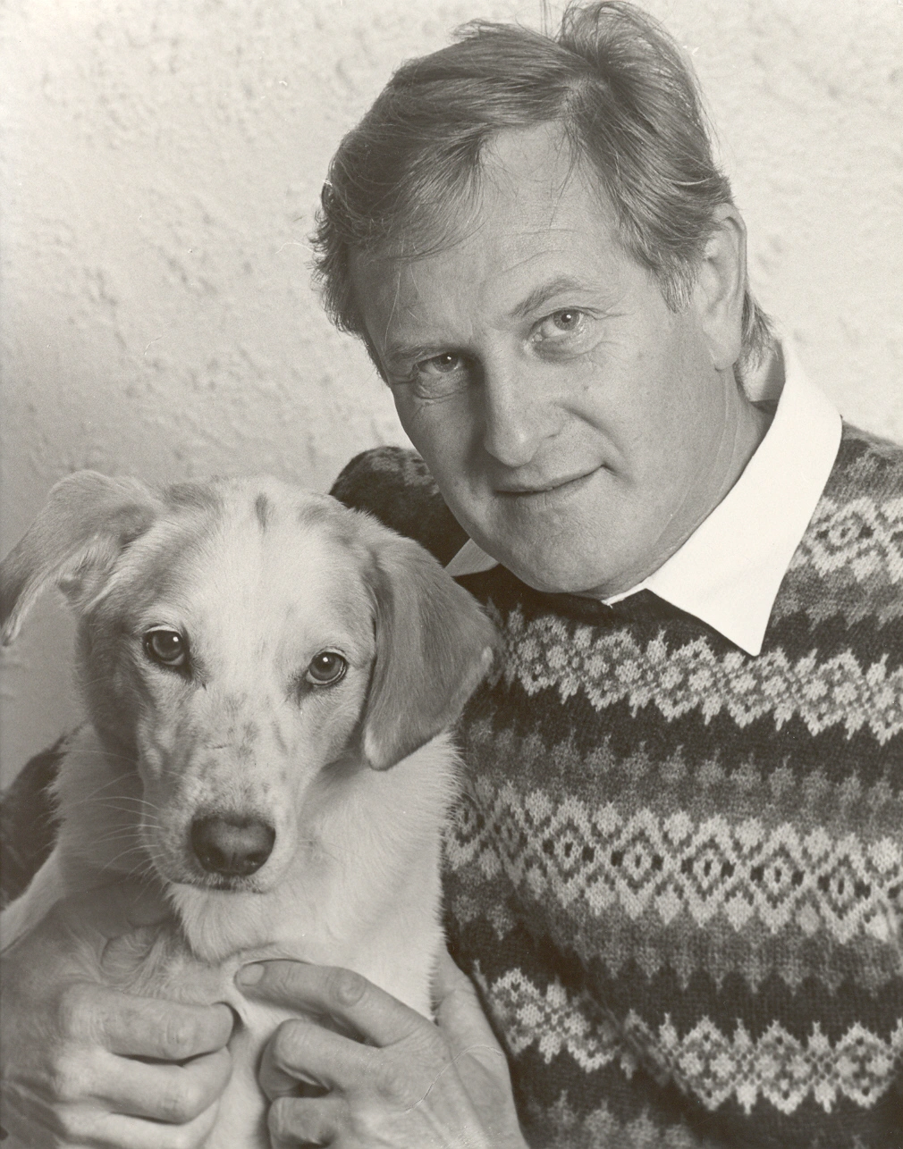 A black and white photo of a man holding a light coloured dog
