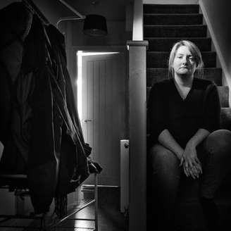 A black and white photo of a woman sitting on stairs in a house. The mood is sombre.