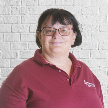 Mid shot of a happy looking woman in Hearing Dogs uniform in front of a white brick wall