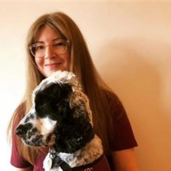 Mid shot of a smiling woman with long hair and glasses with a black and white spaniel in front of her