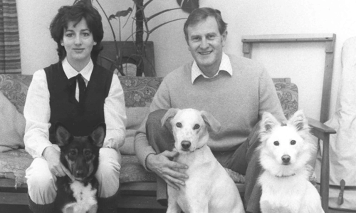 Black and white image of woman and man with three hearing dogs (mixed breeds)