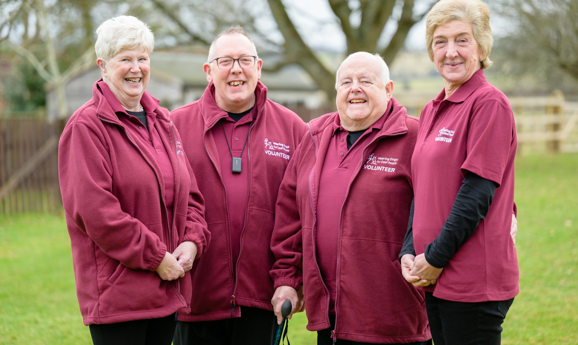 A group of happy looking hearing link services volunteers, stood together outside smiling at the camera