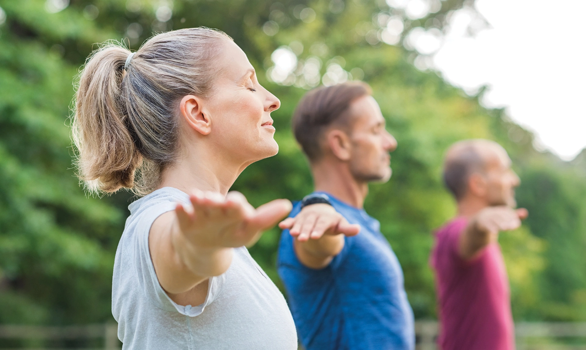 Mid shot of three people stood with their eyes closed and their arms out to their sides
