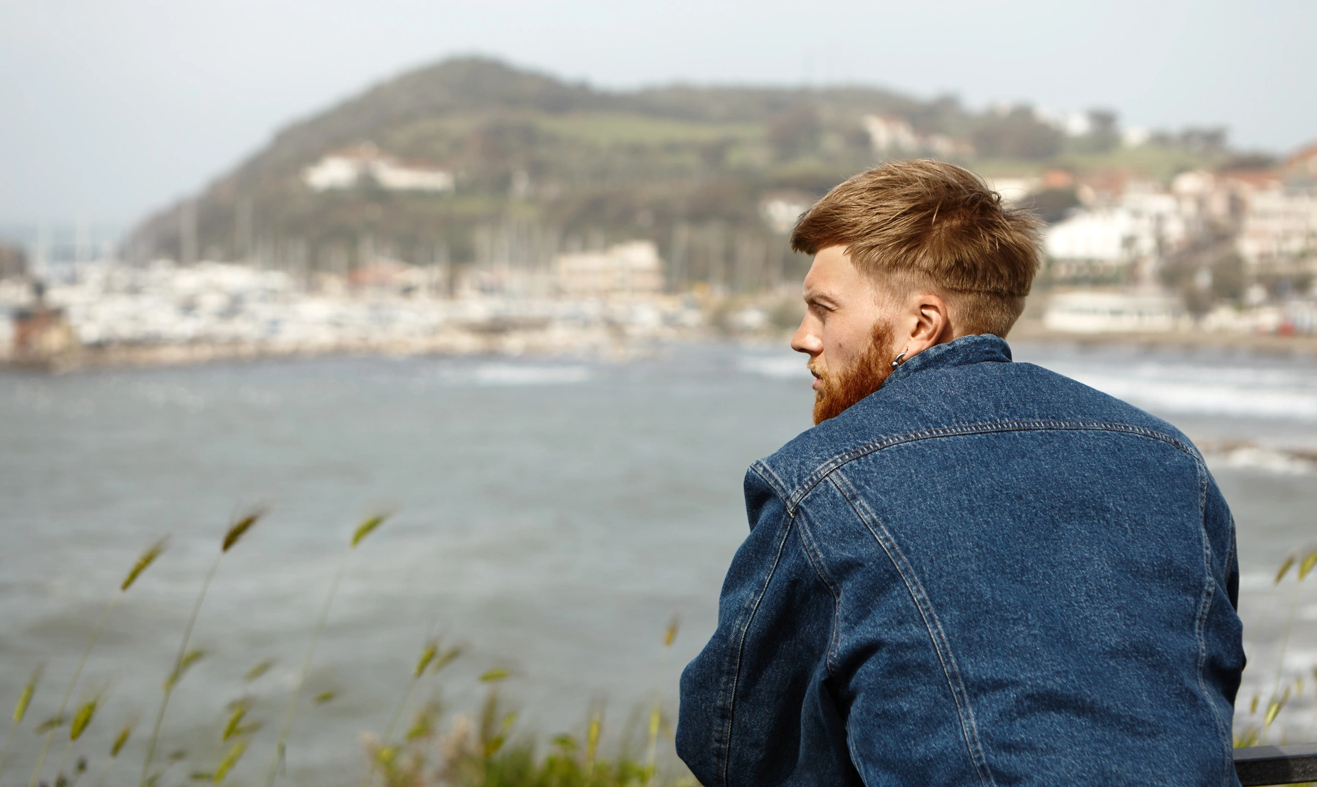 Young man looking thoughtfully out to see with boats and hillside in the distance