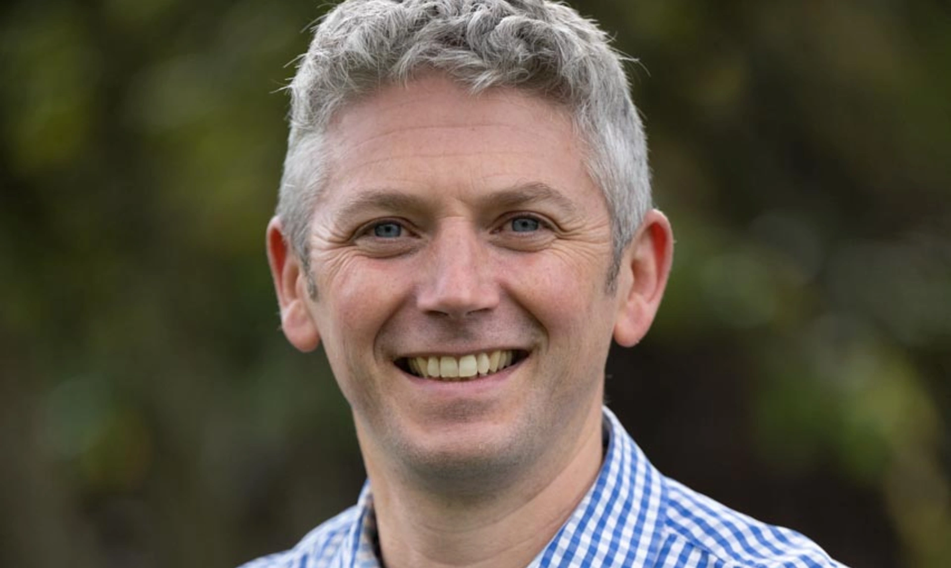 A man smiling in a blue checked shirt