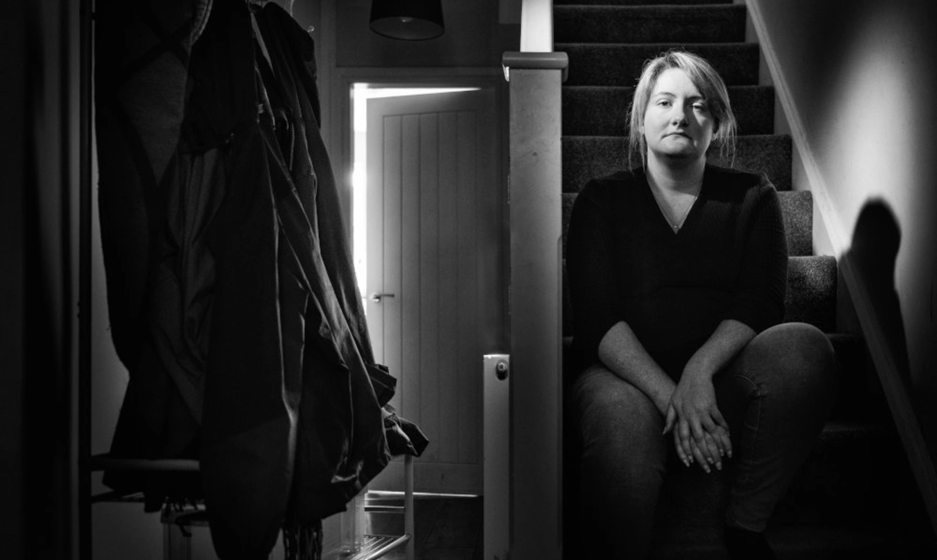 A black and white photo of a woman sitting on stairs in a house. The mood is sombre.