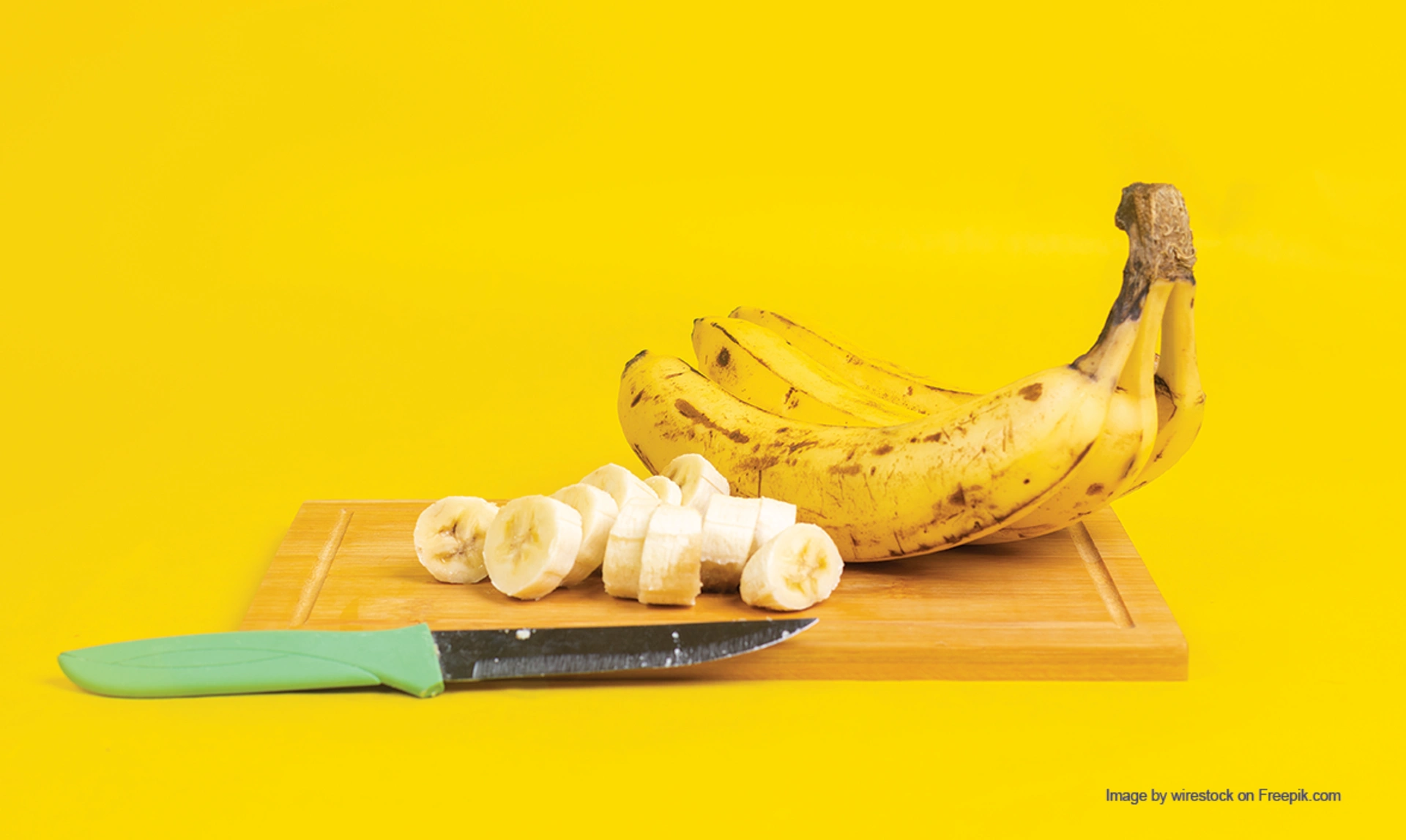 A bunch of bananas and some chopped banana on a wooden board with a knife