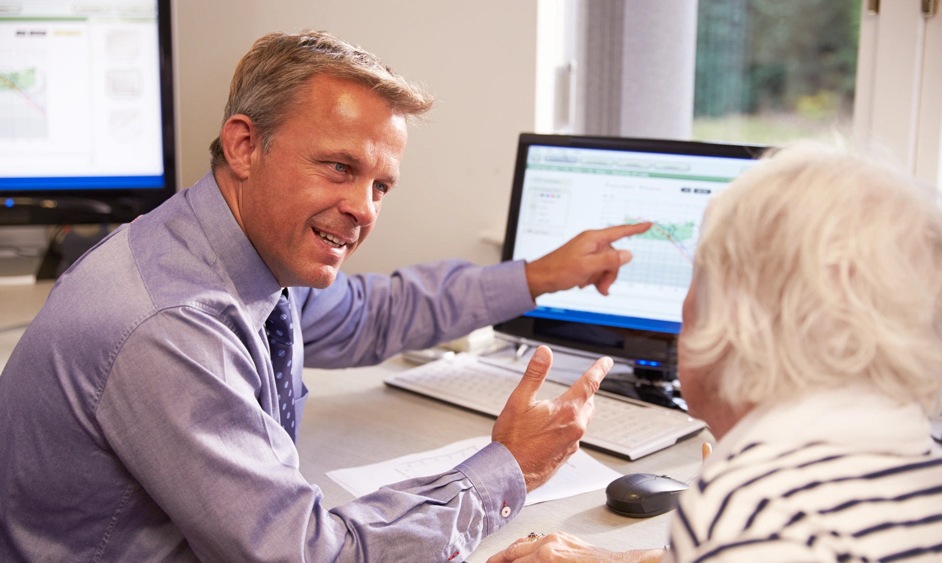 Audiologist sat looking at a patient while he smiles and points to a screen