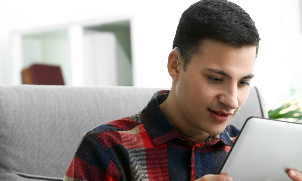 A person sat in a chair with a hearing aid on one ear looking at a screen 