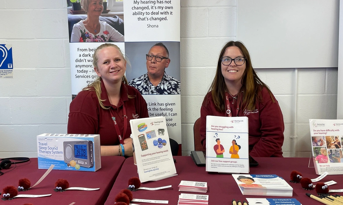 Two people smiling at a table with information and merchandise on it