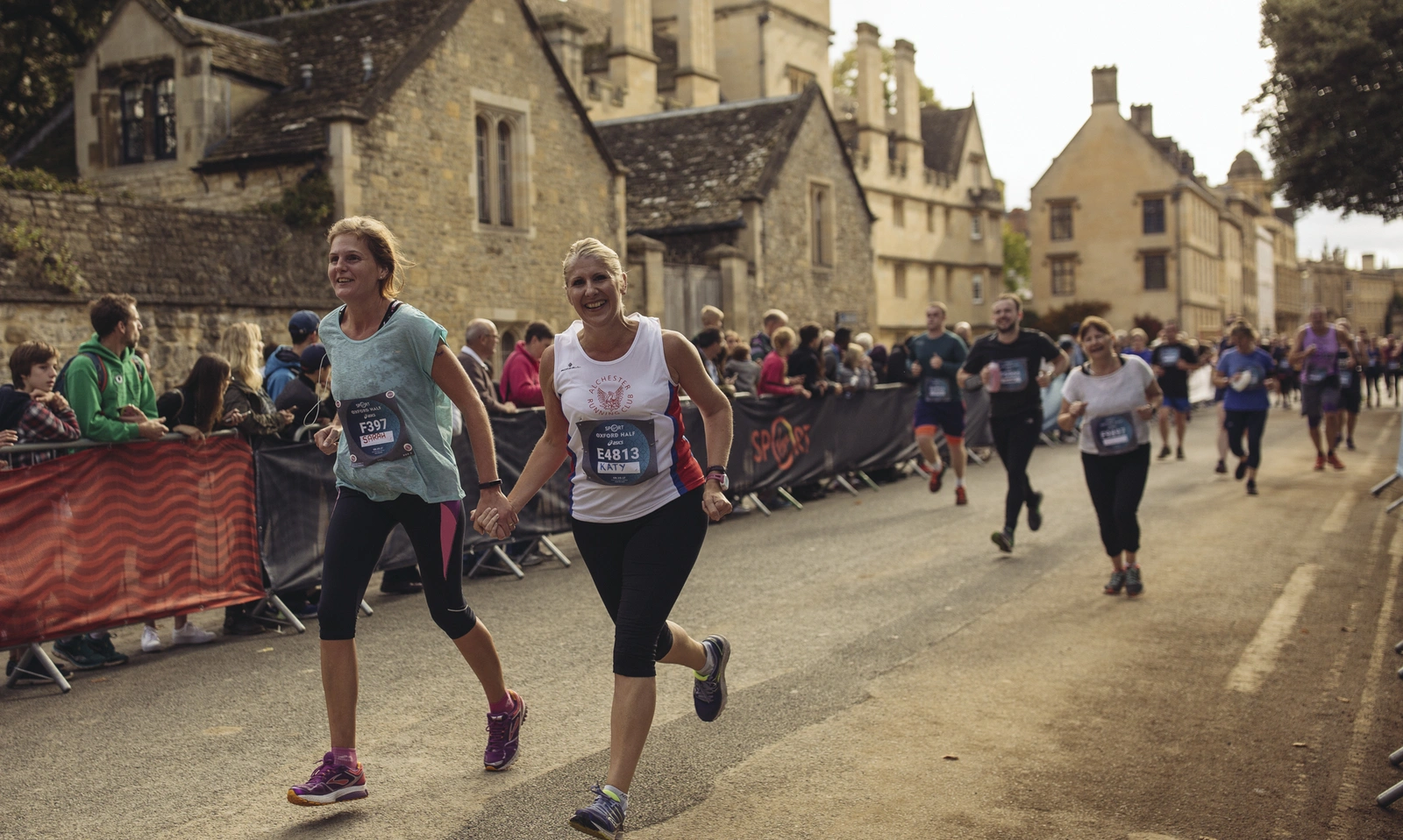 A small group of runners making their way past some old buildings in the background. Central is one female runner in a white shirt, smiling happily.