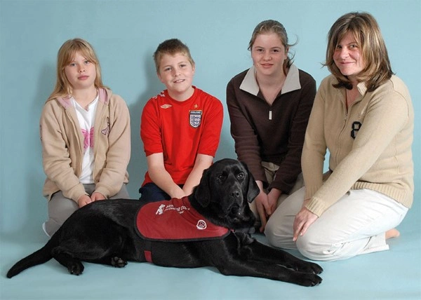 Black Labrador and hearing dog Cara pictured with two woman, a girl and boy
