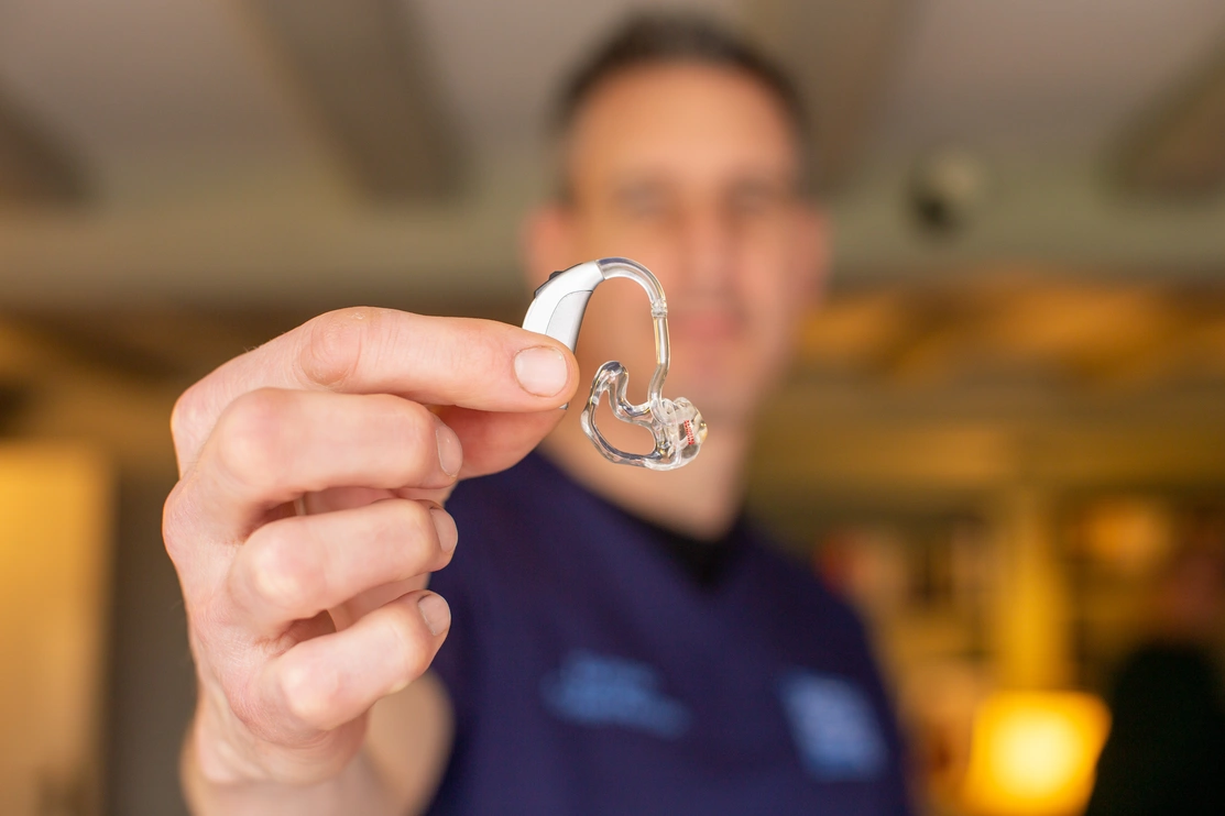 Close up of a hearing aid held by an audiologist, only the hearing aid and audiologist’s hand are in focus the rest of the image is blurry