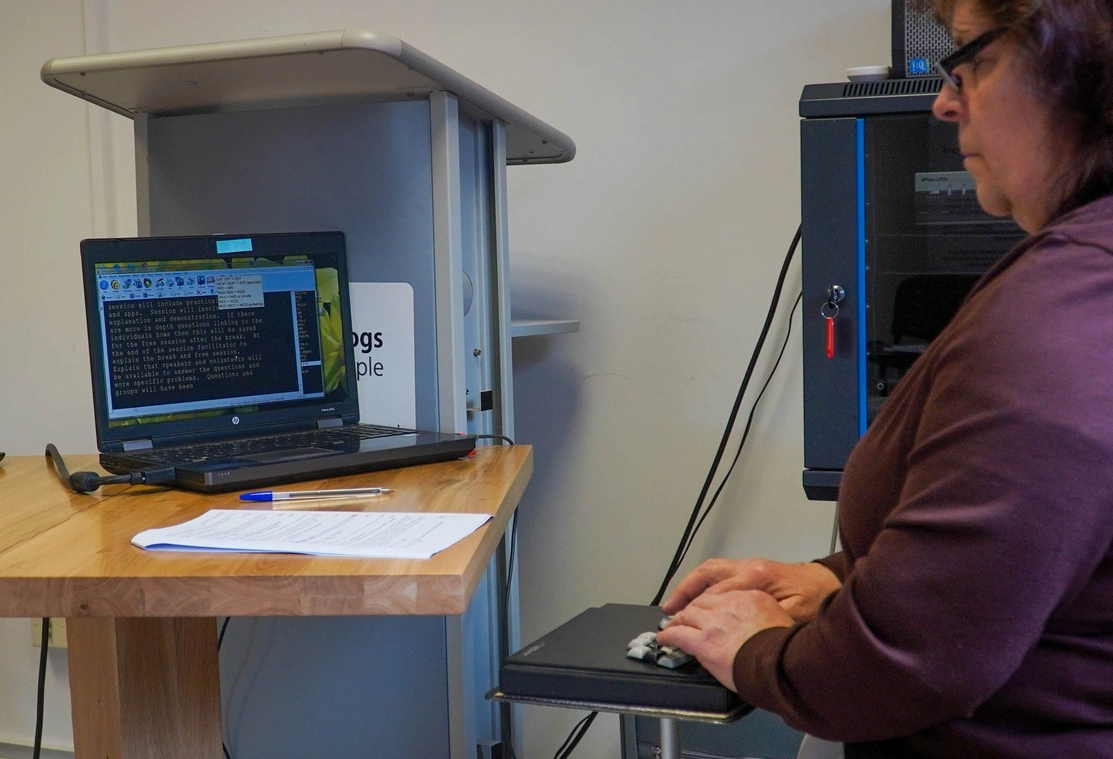 A woman is sat reading a screen which shows speech being transcribed to text