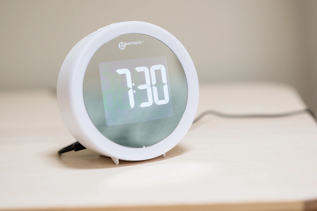 An alarm clock on a table that shows a digital display reading 7:30