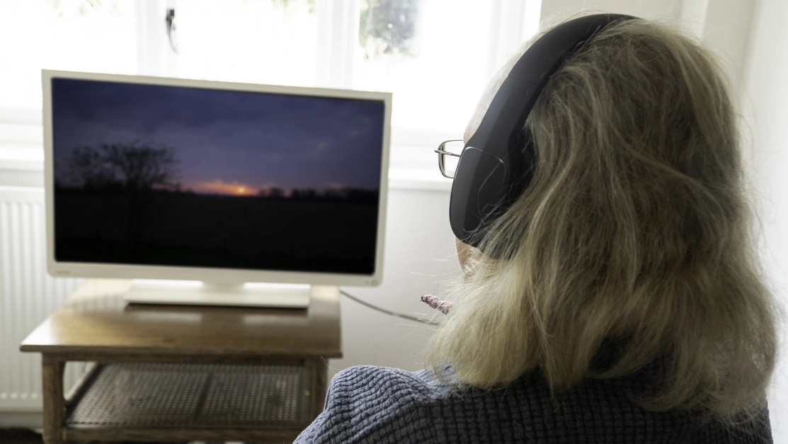 Over the shoulder image of a person sat wearing wireless headphones watching television