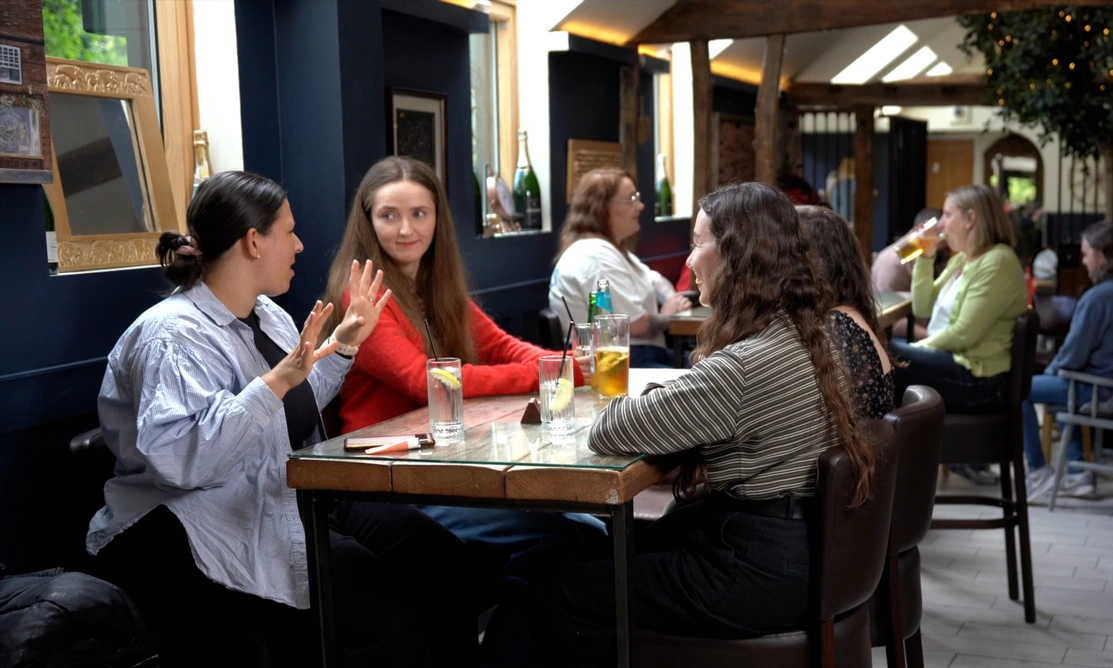 A group of four women sitting at a restaurant table, one is speaking animatedly while the others listen intently..