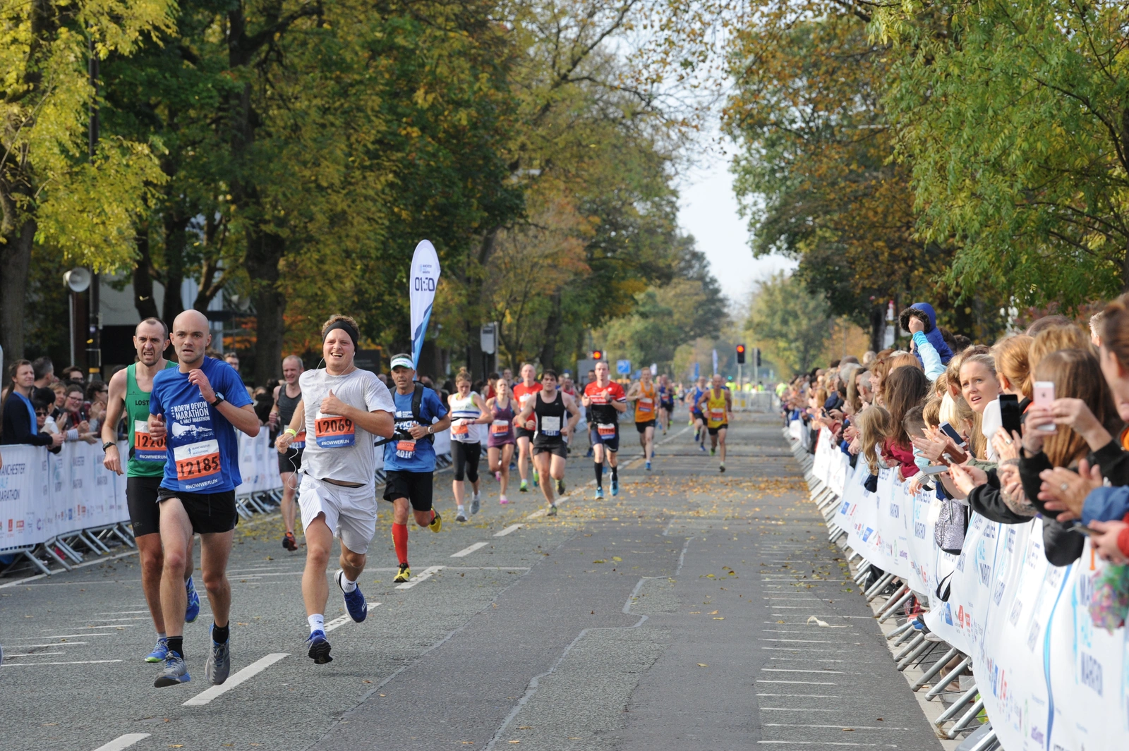 Runners and spectators along a tree lined road, stretching into the far distance.