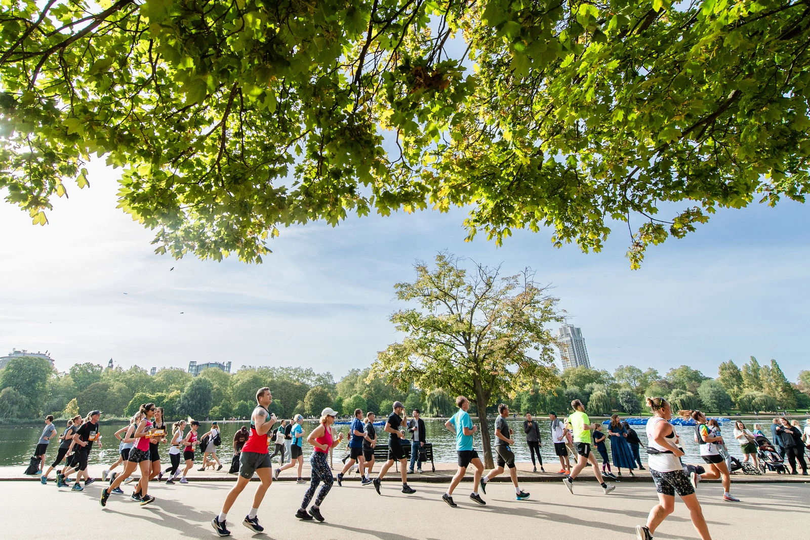 Runners can be seen running alongside the River Thames on a bright sunny day. Tree branches can be seen along the top of the picture.