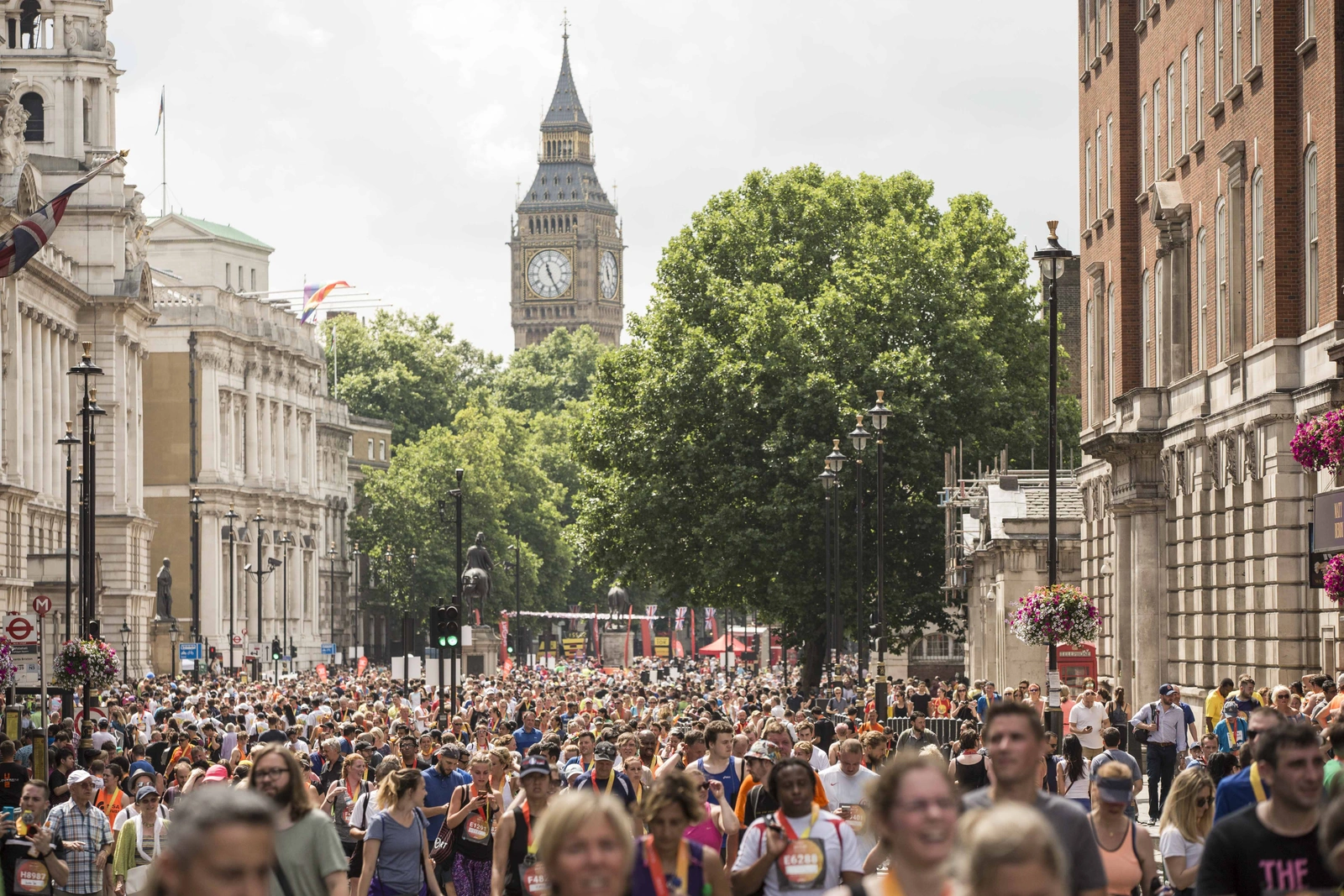 A large crowd of people gathered in London street. Big Ben clocktower can be seen in the background behind some trees.