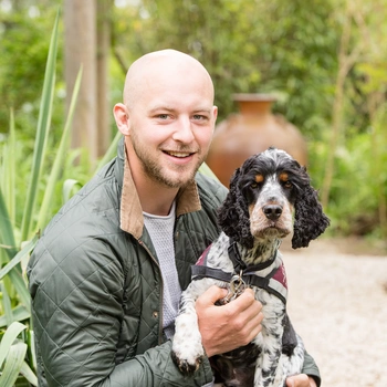 A man sat outside in a garden looking happy with his hearing dog spaniel next to him