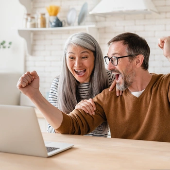 A woman and man happy, cheering with arms in the air infront of a laptop
